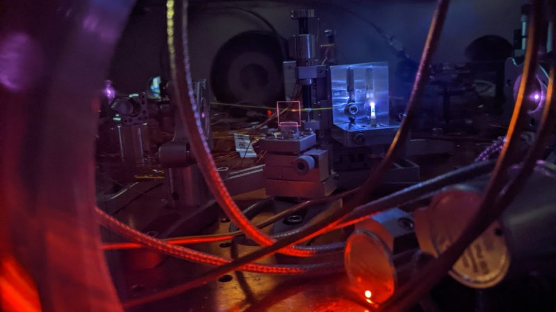 A photograph of scientific equipment, including a laser beam illuminating gas inside a vacuum chamber.